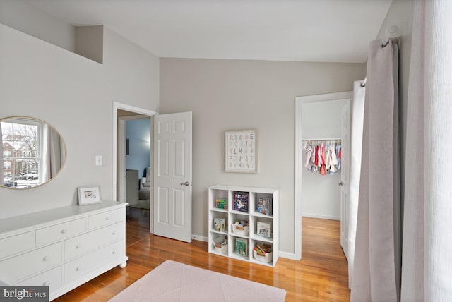 bedroom featuring a walk in closet, a closet, vaulted ceiling, and light hardwood / wood-style floors