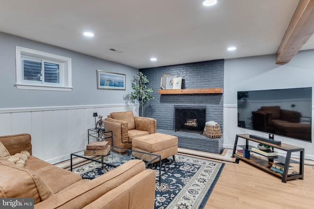 living room featuring beam ceiling, a brick fireplace, and light hardwood / wood-style floors