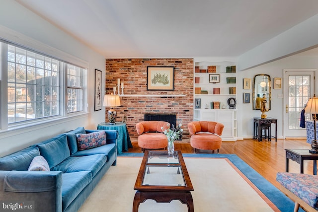 living room featuring built in shelves, a brick fireplace, and light wood-type flooring