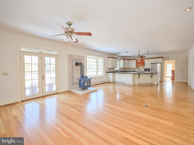 unfurnished living room featuring plenty of natural light, a baseboard heating unit, a wood stove, and light wood-type flooring