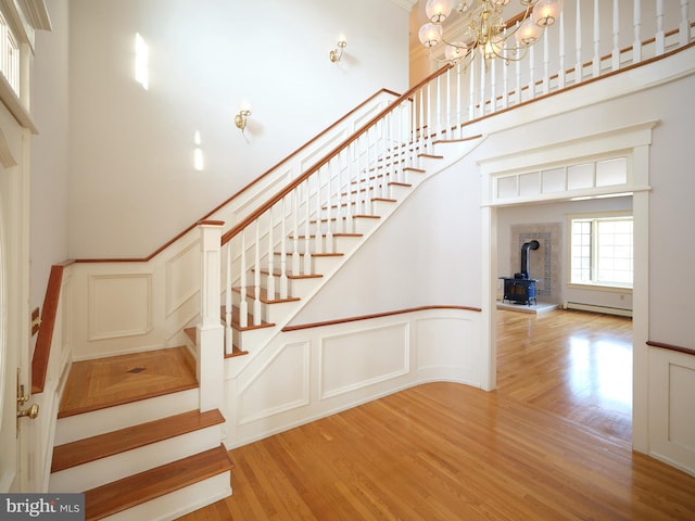 staircase featuring baseboard heating, a wood stove, hardwood / wood-style flooring, and an inviting chandelier