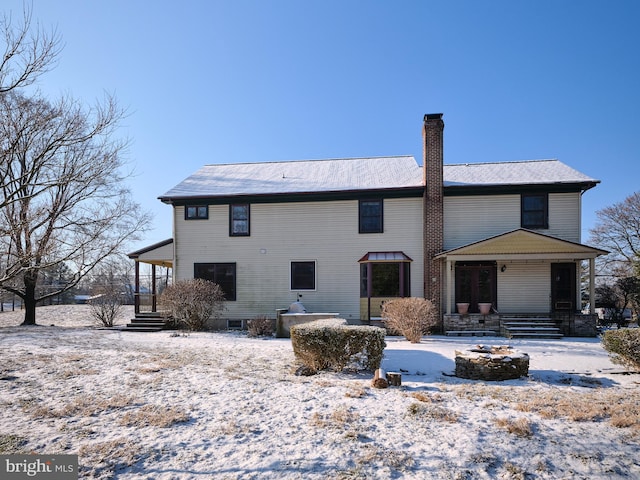 snow covered back of property with covered porch and an outdoor fire pit