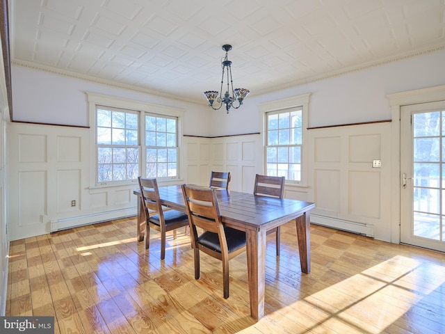 dining space with a baseboard heating unit, an inviting chandelier, ornamental molding, and light wood-type flooring