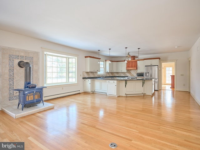 kitchen with decorative light fixtures, a kitchen bar, appliances with stainless steel finishes, a wood stove, and baseboard heating