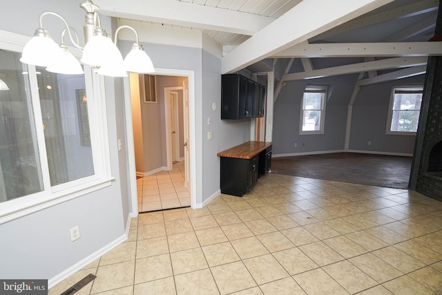 interior space featuring hanging light fixtures, light tile patterned floors, a notable chandelier, butcher block countertops, and beam ceiling