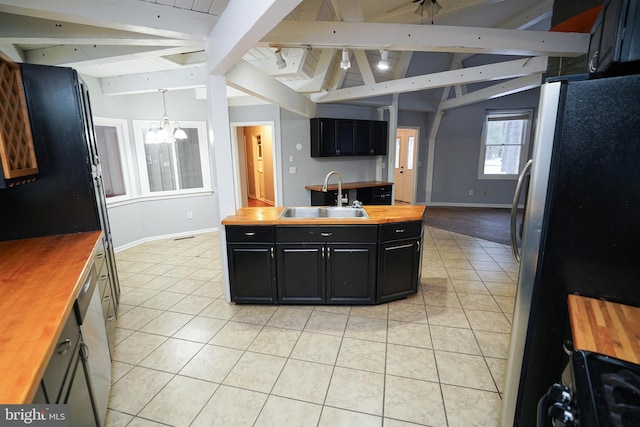 kitchen featuring appliances with stainless steel finishes, vaulted ceiling with beams, a notable chandelier, sink, and butcher block counters