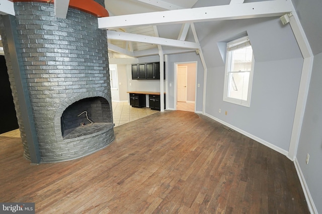 unfurnished living room featuring light wood-type flooring, lofted ceiling with beams, and a fireplace