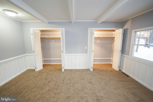 unfurnished bedroom featuring light carpet, multiple closets, ornamental molding, and beam ceiling