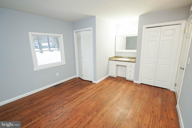 unfurnished bedroom with sink, light hardwood / wood-style floors, two closets, and built in desk