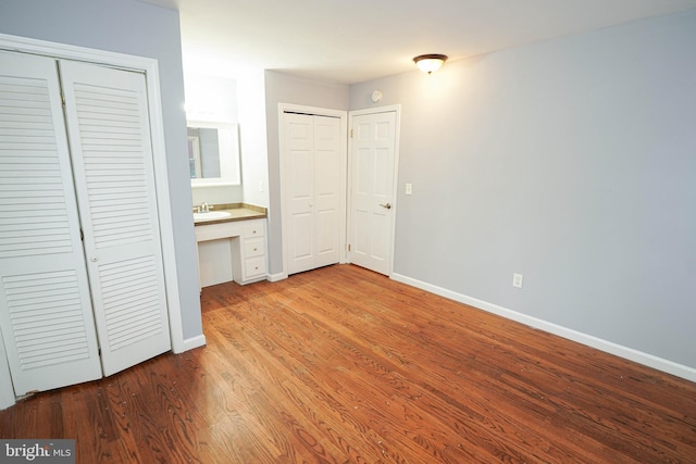 unfurnished bedroom with built in desk, multiple closets, sink, light hardwood / wood-style flooring, and ensuite bathroom