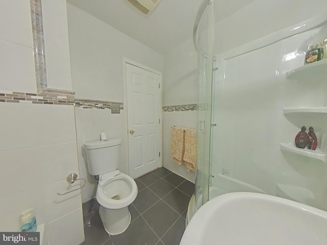 bathroom with toilet, tile patterned flooring, a shower with door, and tile walls