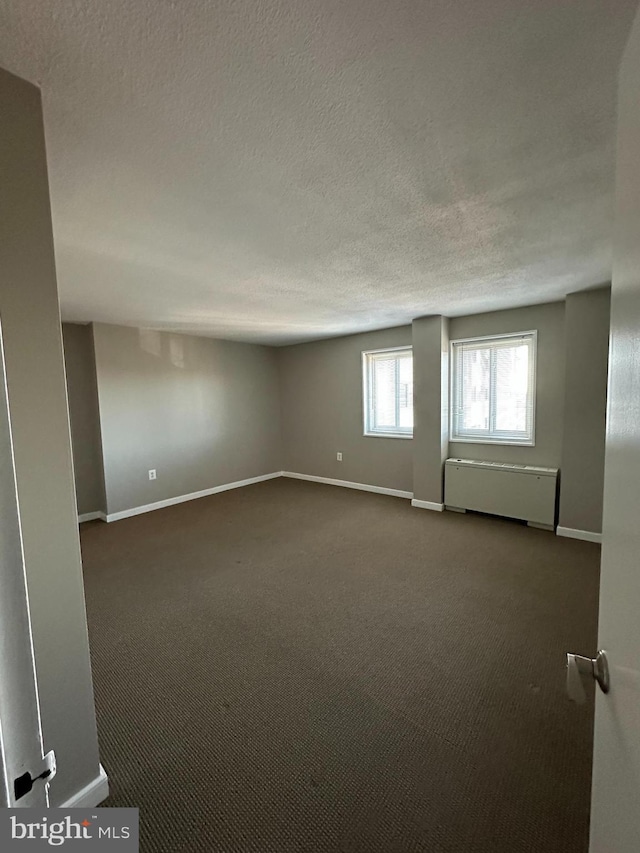 spare room featuring radiator heating unit, a textured ceiling, and dark colored carpet