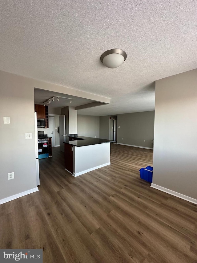 kitchen featuring rail lighting, stainless steel appliances, a textured ceiling, dark hardwood / wood-style flooring, and kitchen peninsula