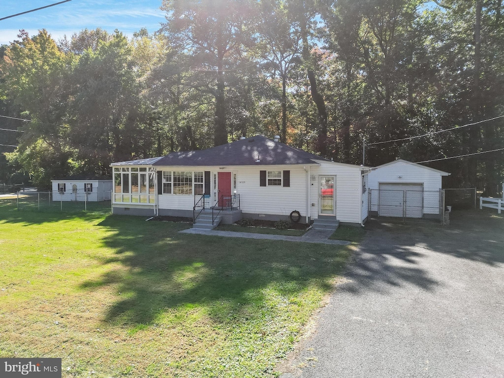 view of front of property featuring a front yard, a garage, an outbuilding, and a sunroom