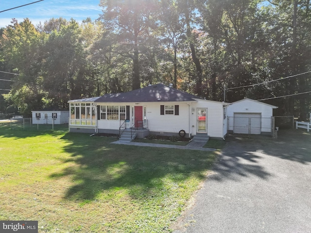 view of front of property featuring a front yard, a garage, an outbuilding, and a sunroom