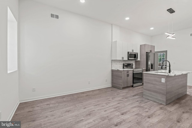 kitchen featuring pendant lighting, stainless steel appliances, sink, a kitchen island with sink, and light wood-type flooring