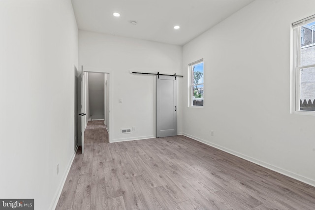 unfurnished bedroom with a barn door and light wood-type flooring