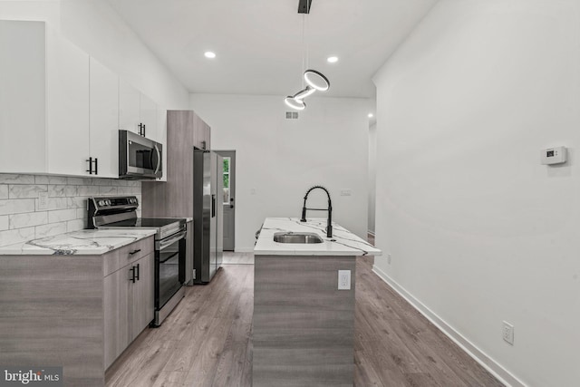 kitchen with an island with sink, stainless steel appliances, pendant lighting, white cabinets, and sink