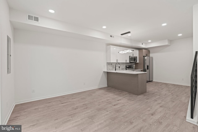 kitchen featuring kitchen peninsula, appliances with stainless steel finishes, light wood-type flooring, hanging light fixtures, and white cabinets