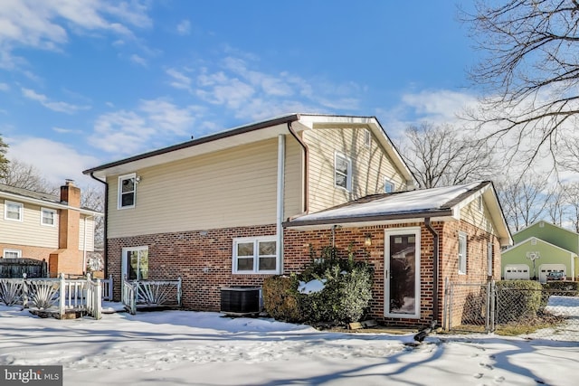 snow covered house with central AC unit and a garage