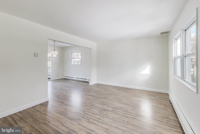 spare room featuring baseboard heating, hardwood / wood-style floors, and an inviting chandelier