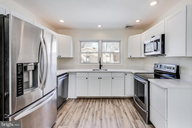 kitchen with sink, white cabinets, appliances with stainless steel finishes, and light hardwood / wood-style flooring