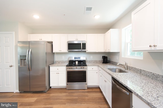 kitchen with light stone counters, stainless steel appliances, light hardwood / wood-style floors, white cabinets, and sink