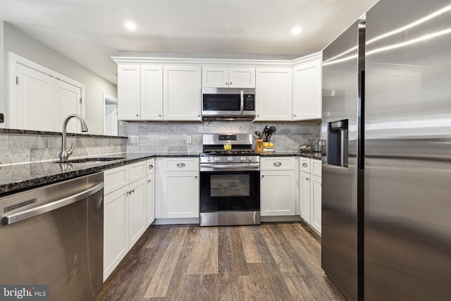 kitchen with appliances with stainless steel finishes, dark stone counters, white cabinets, and sink