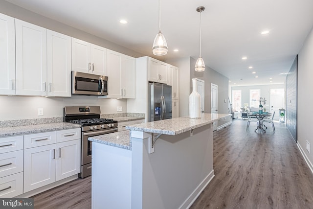 kitchen featuring white cabinets, a kitchen island, dark hardwood / wood-style flooring, pendant lighting, and appliances with stainless steel finishes