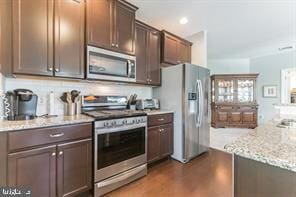 kitchen featuring stainless steel appliances, light stone countertops, and dark brown cabinetry