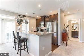 kitchen with a breakfast bar, stainless steel appliances, light carpet, and dark brown cabinetry