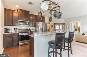 kitchen featuring light stone countertops, an island with sink, a breakfast bar area, appliances with stainless steel finishes, and dark brown cabinetry