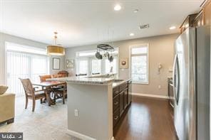 kitchen featuring stainless steel fridge, a kitchen island with sink, plenty of natural light, and hanging light fixtures