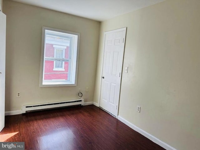 empty room with baseboard heating and dark hardwood / wood-style floors