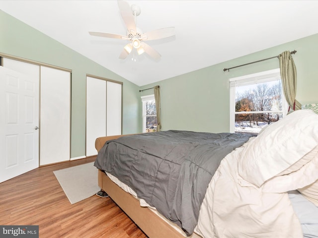 bedroom featuring lofted ceiling, multiple windows, multiple closets, and light wood-type flooring