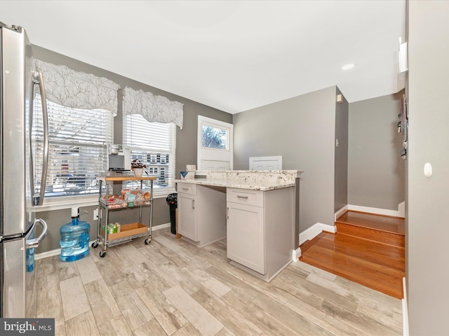 kitchen featuring white cabinetry, stainless steel fridge, light stone countertops, and light wood-type flooring