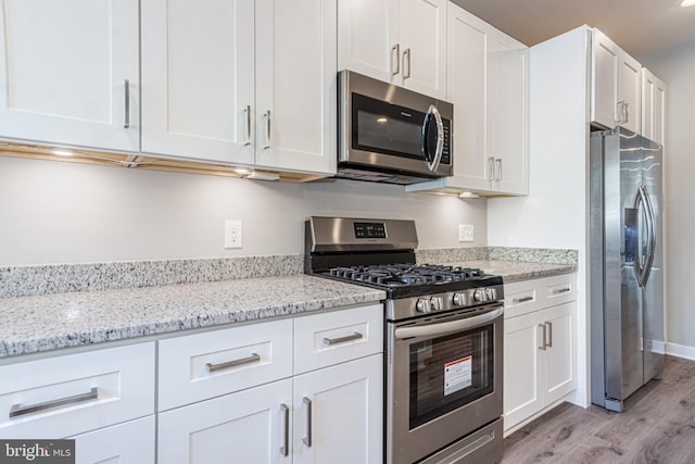 kitchen with light hardwood / wood-style floors, light stone countertops, white cabinets, and stainless steel appliances