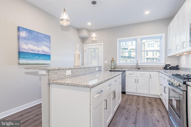 kitchen featuring appliances with stainless steel finishes, wood-type flooring, white cabinetry, sink, and hanging light fixtures