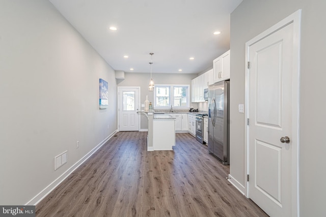 kitchen with pendant lighting, a kitchen island, hardwood / wood-style flooring, stainless steel appliances, and white cabinets