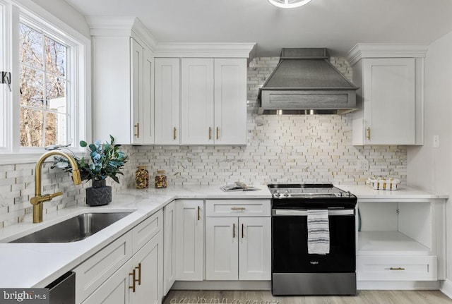 kitchen with stainless steel range with electric cooktop, custom range hood, sink, and white cabinets