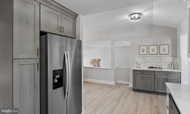 kitchen featuring stainless steel fridge with ice dispenser, light stone counters, lofted ceiling, light hardwood / wood-style flooring, and backsplash