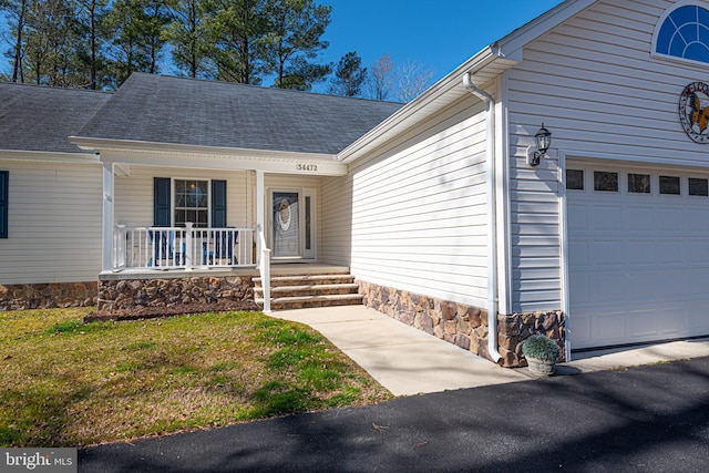 doorway to property featuring covered porch, a lawn, and a garage