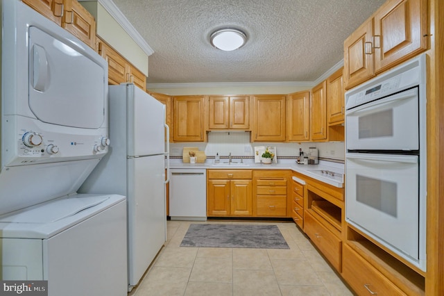 kitchen with sink, stacked washer / drying machine, light tile patterned floors, crown molding, and white appliances