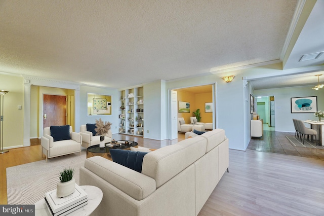 living room with crown molding, decorative columns, light hardwood / wood-style floors, and a textured ceiling