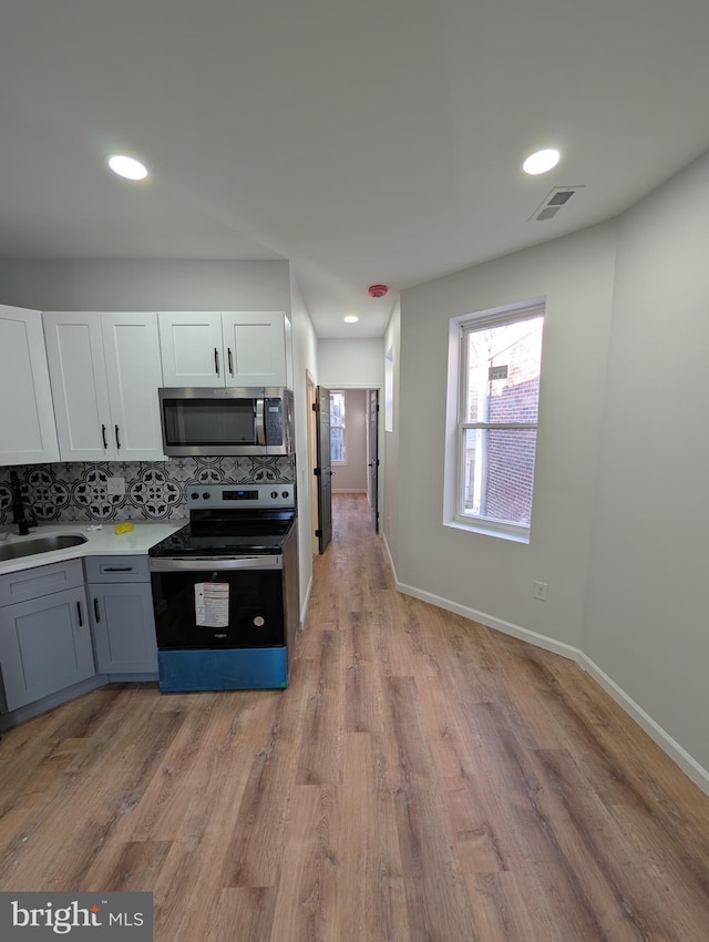 kitchen with stainless steel appliances, backsplash, white cabinets, light hardwood / wood-style flooring, and sink