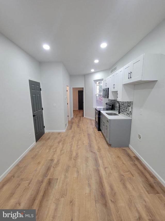 kitchen with white cabinets, sink, backsplash, black electric range oven, and light hardwood / wood-style flooring