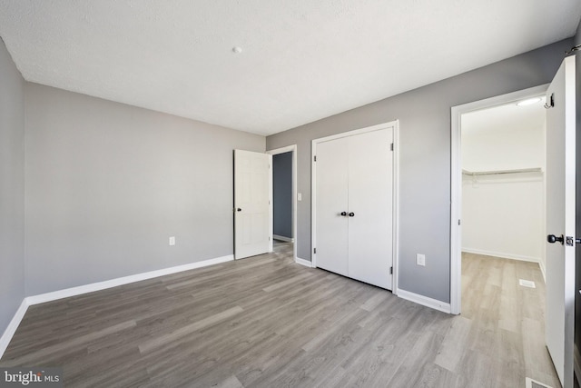 unfurnished bedroom featuring a walk in closet, light hardwood / wood-style flooring, and a textured ceiling