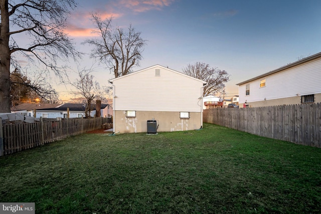 back house at dusk featuring central air condition unit and a lawn