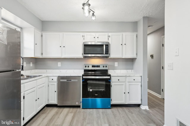 kitchen with white cabinetry, appliances with stainless steel finishes, a textured ceiling, and light wood-type flooring