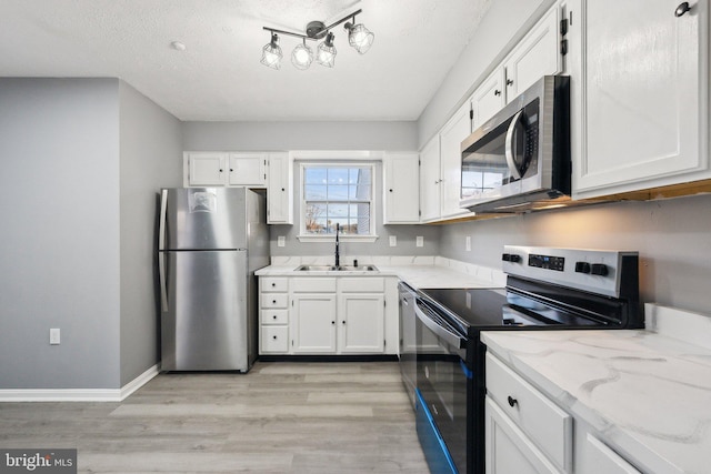 kitchen with sink, white cabinetry, light stone counters, light hardwood / wood-style flooring, and appliances with stainless steel finishes